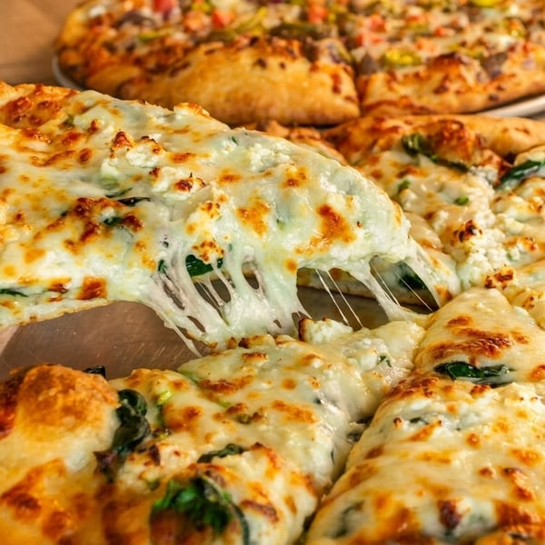 A slice of white pizza with spinach and ricotta is lifted, showing stretchy cheese.