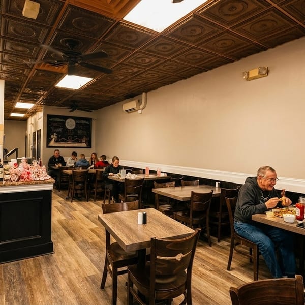 Diners enjoy meals at wooden tables in a casual restaurant with a decorative ceiling and counter.