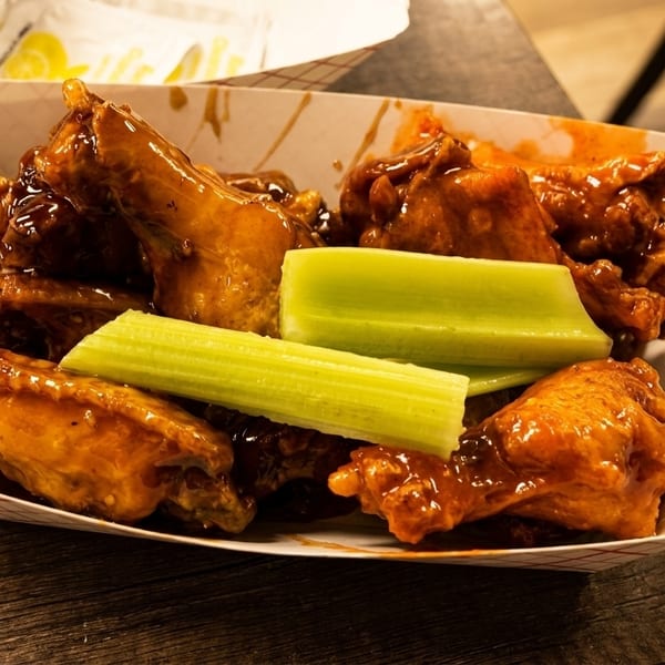 A paper tray filled with glossy, sauced chicken wings and several crisp celery sticks.